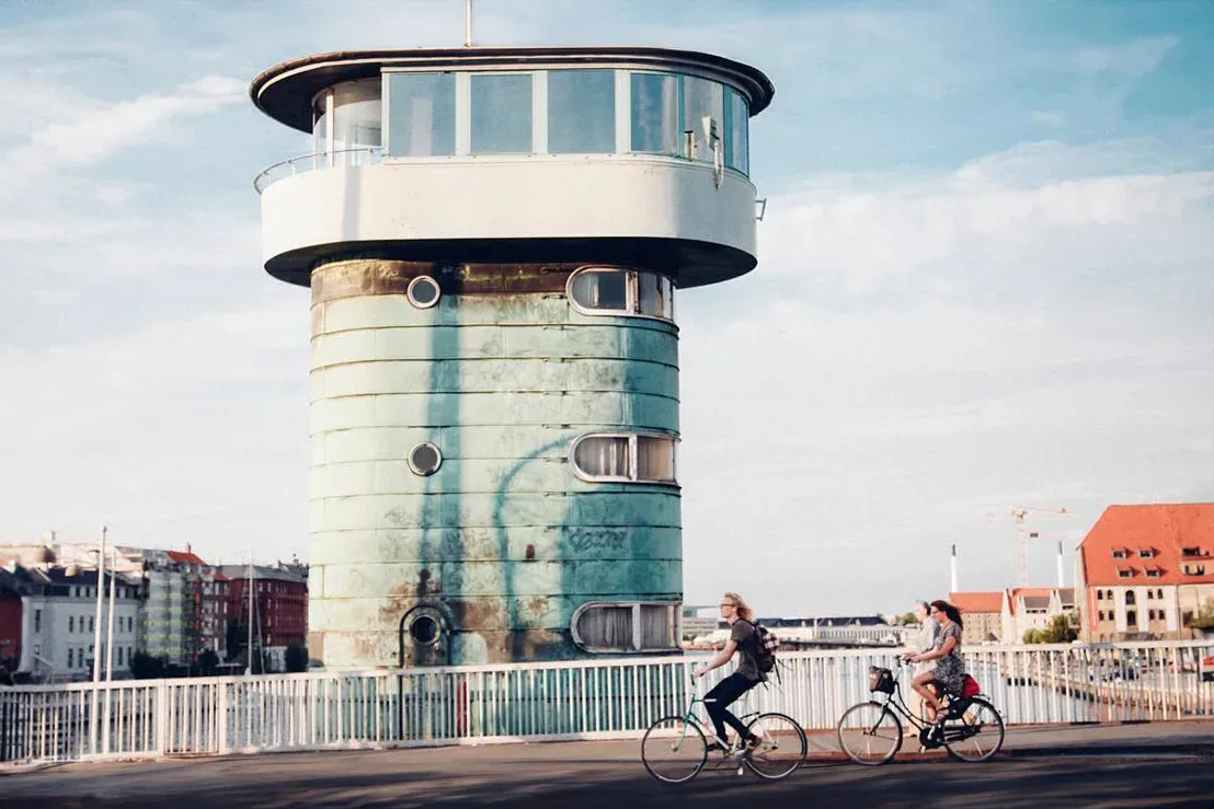 Two people riding bicycles in front of a water tower.