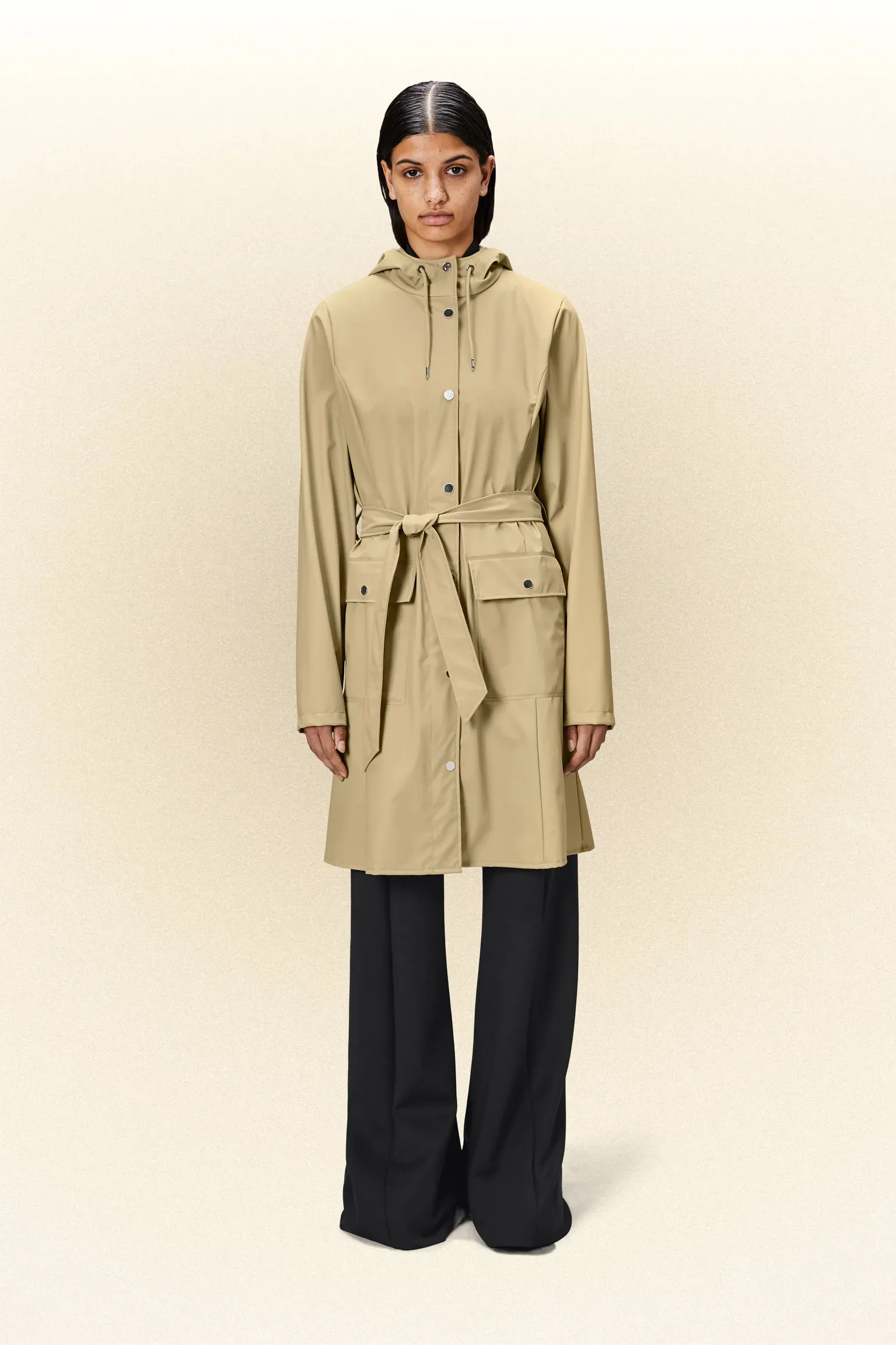 A woman wearing a beige trench coat and black pants.