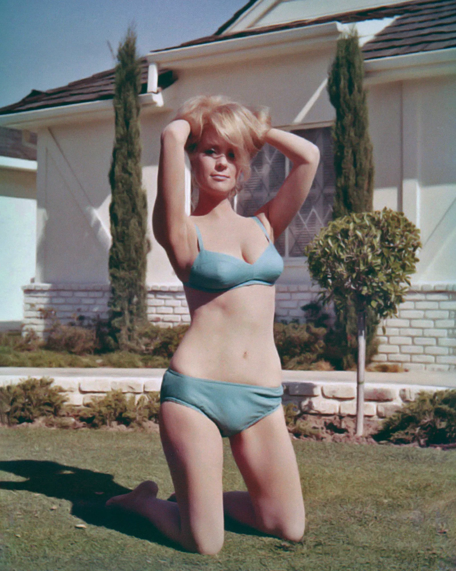 A woman in a blue bikini posing in front of a house, keyword: bikini.