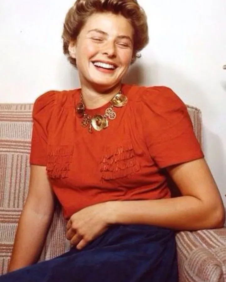 A smiling woman, Ingrid Bergman, sitting on a couch.