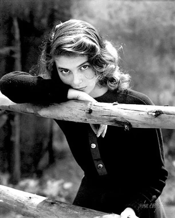 A black and white photo of Ingrid Bergman leaning against a wooden fence.