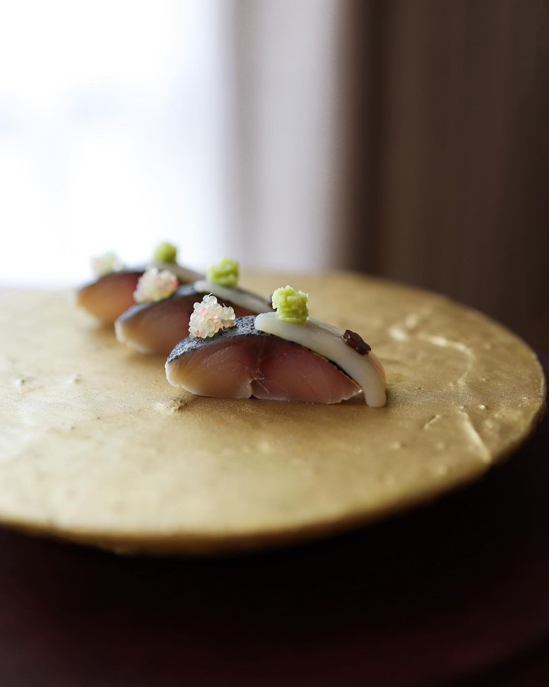 Three pieces of sashimi at a Copenhagen restaurant on a gold plate.