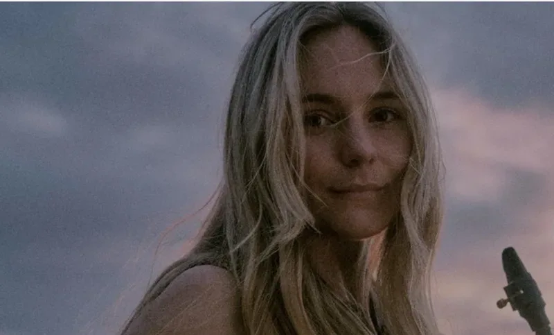 A woman with long blonde hair holding a guitar.