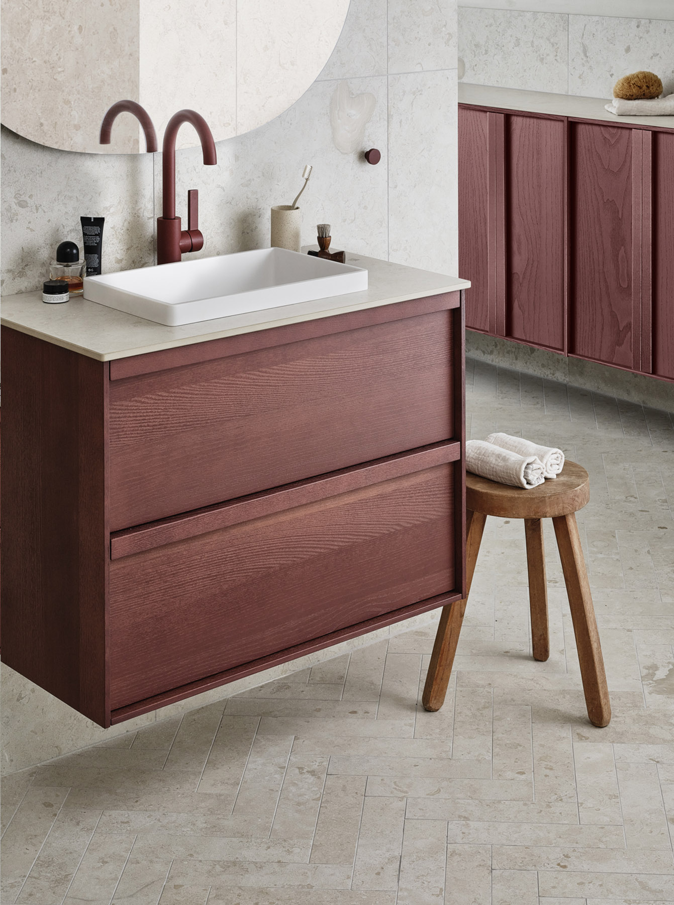 A modern bathroom featuring a floating wooden vanity, white rectangular sink, red faucet, and a stool with towels. The floor and walls are tiled in neutral colors complemented by Toniton paints, while a large mirror adds to the spacious feel.