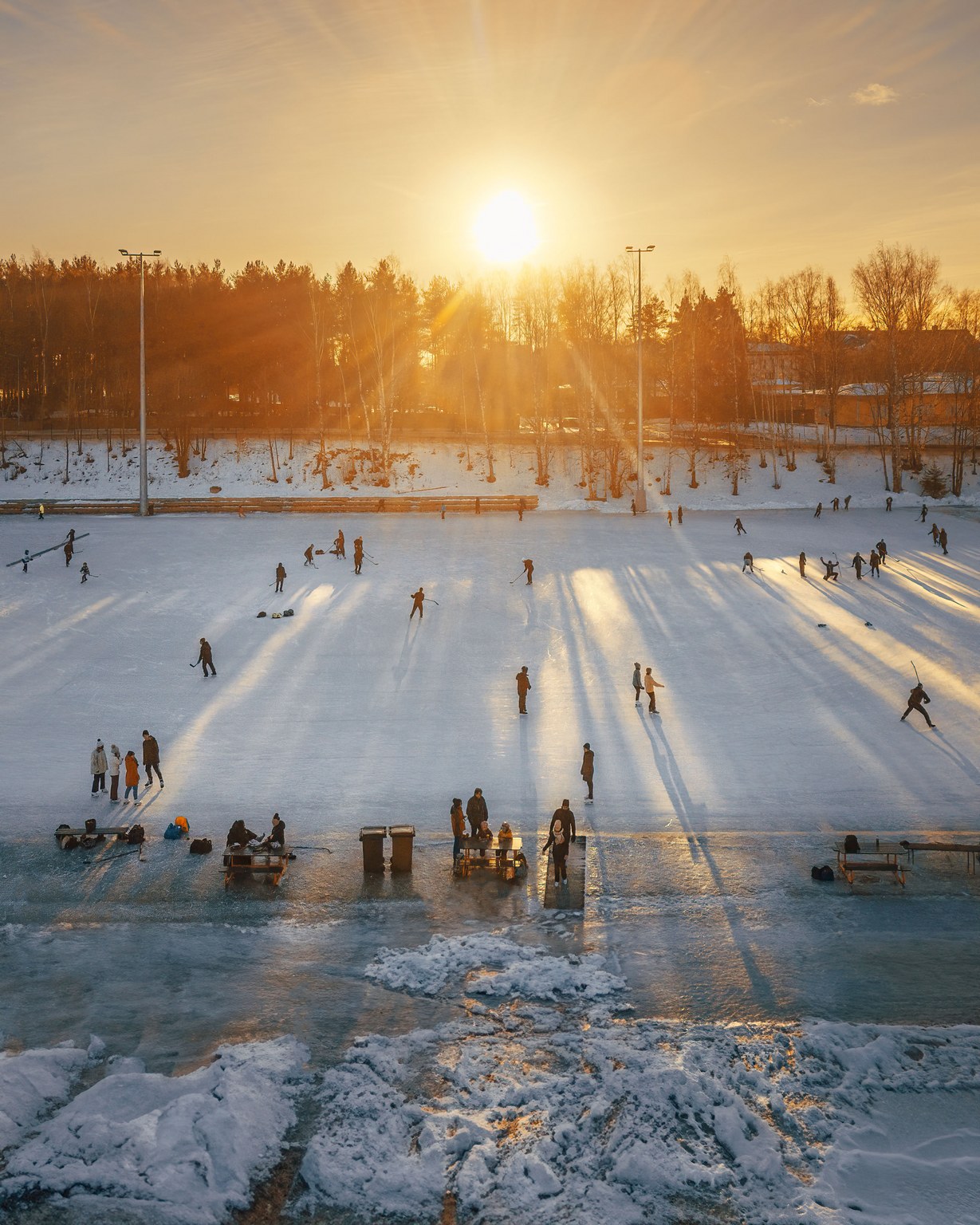 People ice skating in Duck Park Sorsapuisto at sunset, surrounded by trees and snowy ground.