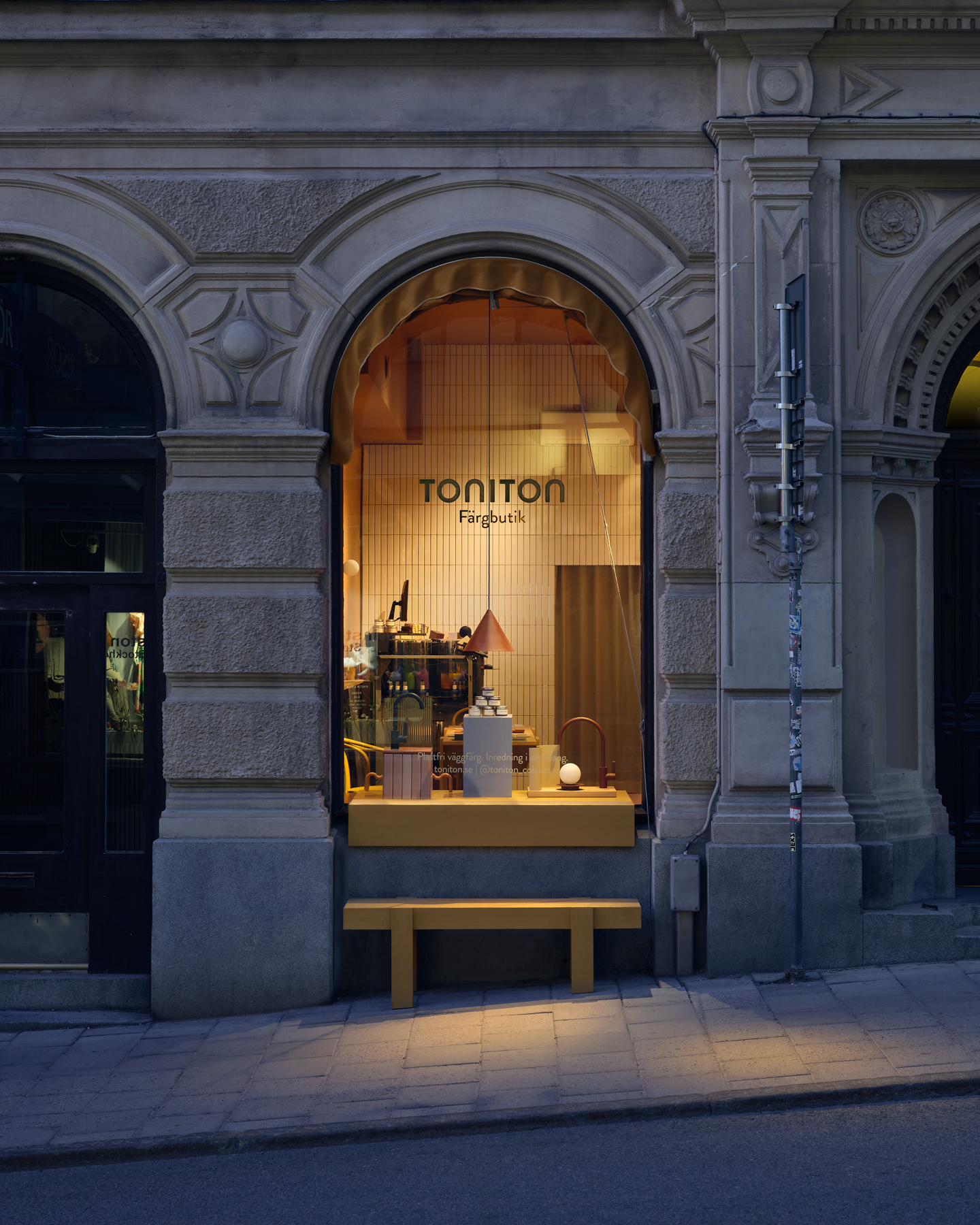 A warmly lit store window labeled "Toniton Paint Boutique" with various items on display, framed by arched architecture on a quiet street in Stockholm.
