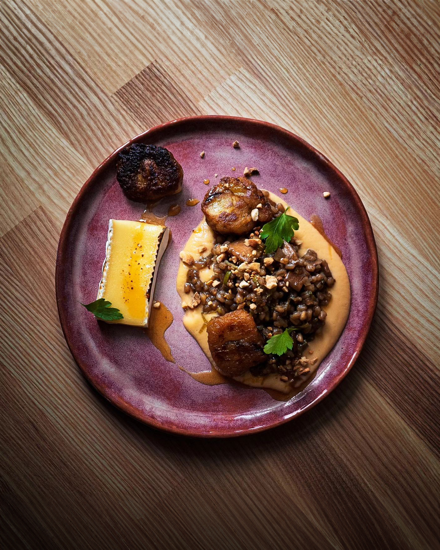 A purple plate containing seared scallops, a creamy sauce, and a side of lentils garnished with herbs and crushed nuts, alongside a rectangular piece of crème brûlée.