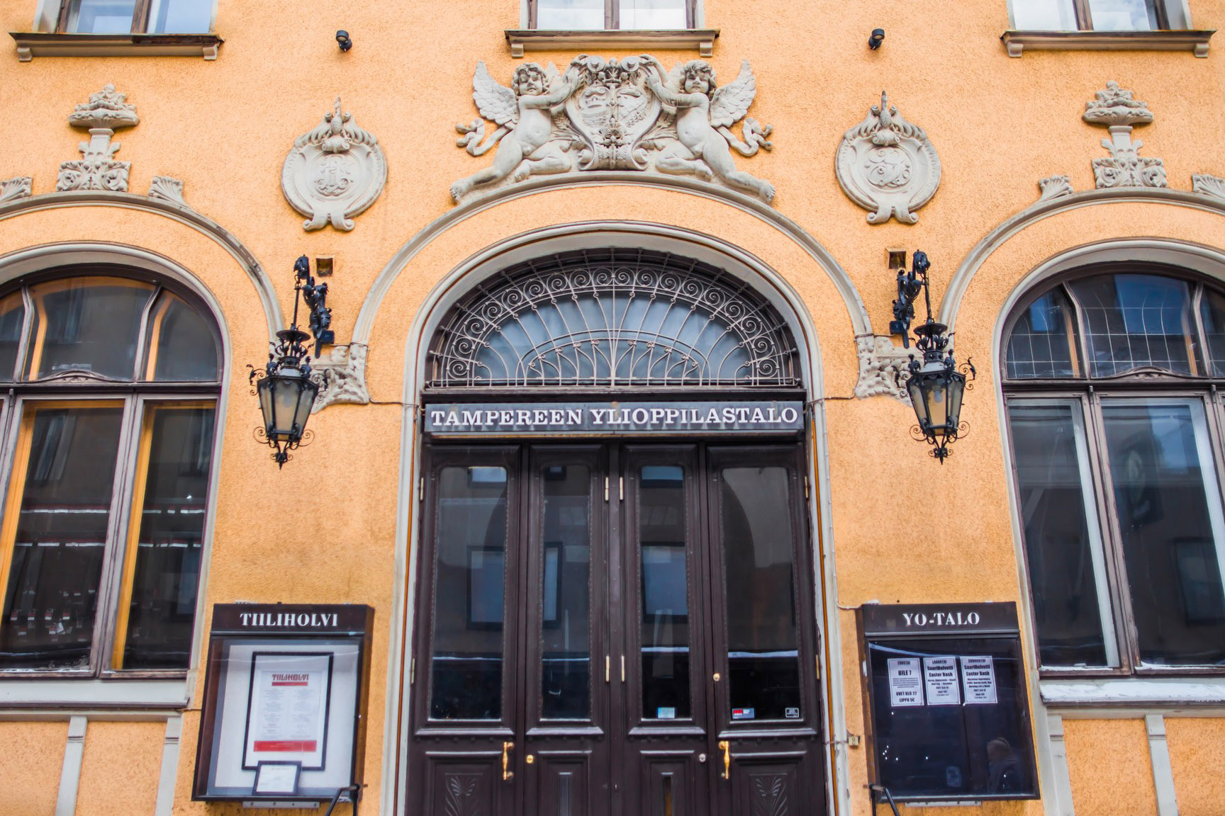 The entrance of Tampereen Ylioppilastalo, an old university bar known as Yo-Talo, features ornate architectural details, two lanterns, and signs labeled "Tillihovi" and "Yo-Talo.