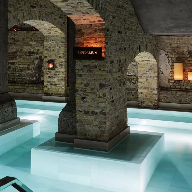 A serene indoor spa with stone arches and softly lit pools of water, creating a tranquil atmosphere.