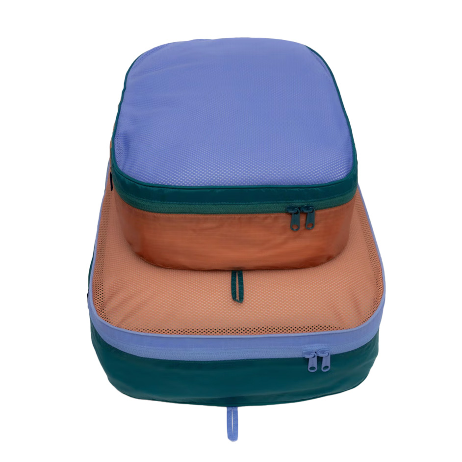 Two stacked rectangular packing cubes, one purple on top of an orange one, both with zippers and green trim.