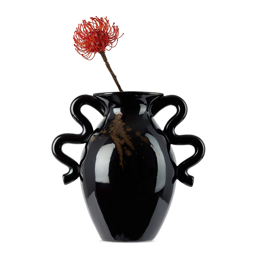 A black ceramic vase with three curvy handles on each side, holding a single red-orange flower.
