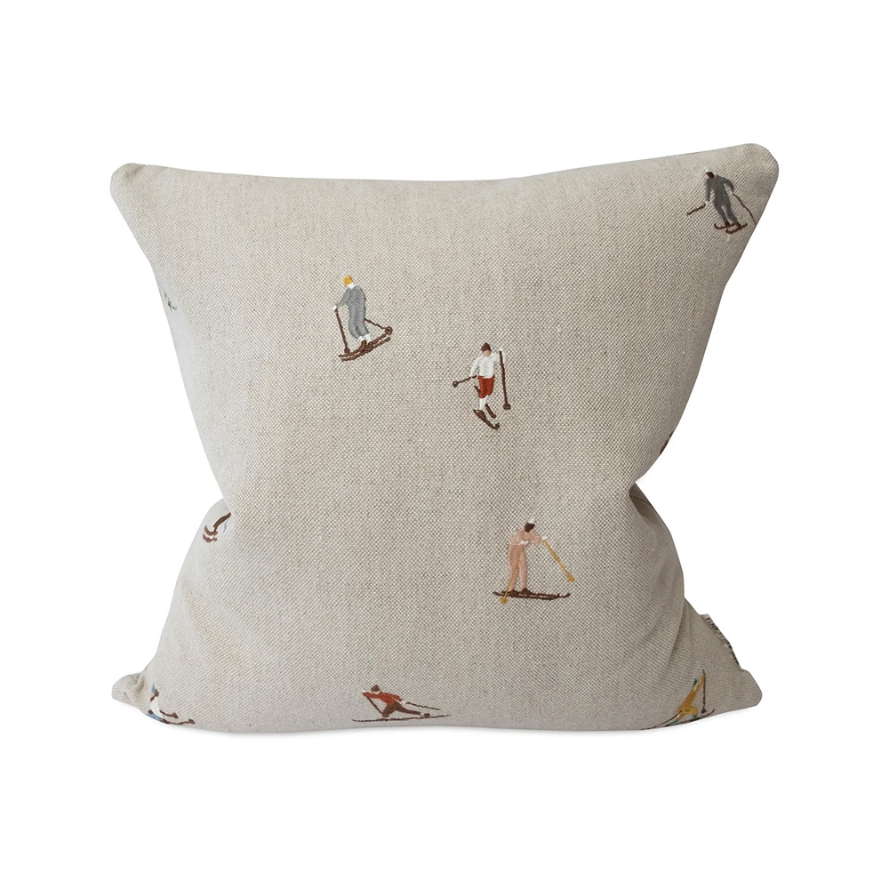 A square pillow with a beige background featuring small, scattered illustrations of skiers in various poses.