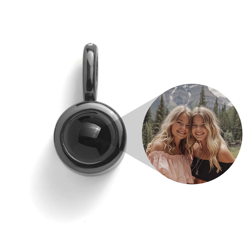 A small black charm with an image inside of loved ones: two smiling women outdoors in a forest setting.