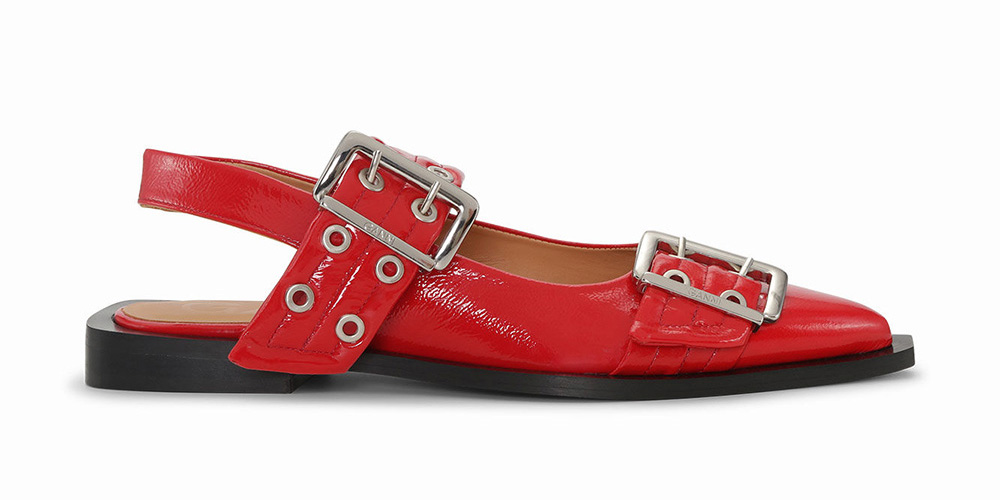 Red leather flat shoe with a pointed toe and two silver buckle straps.