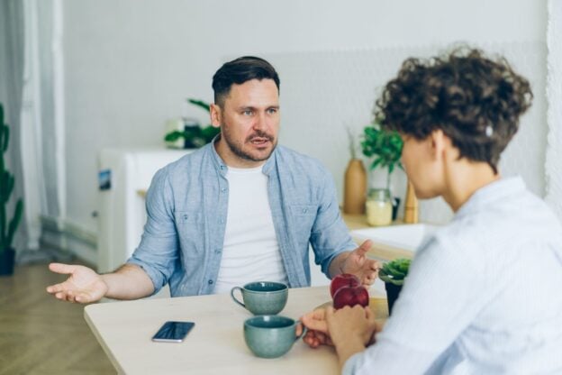Two adults having a calm conversation at a kitchen table with coffee cups, a representative image, not a photograph of any person discussed in the article.