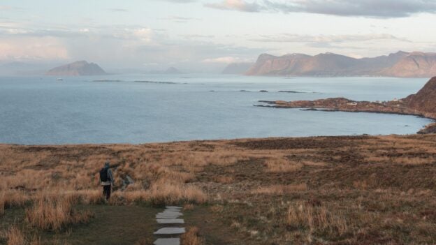 A lone hiker following a path towards a broad coastal view at Runde, Norway
