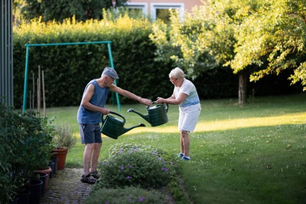 An older couple watering plants together in a sunny garden