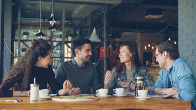 Four friends listening and talking together around a café table